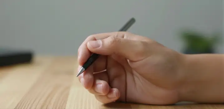 Hand Holding Black Stylus Pen on Wooden Surface