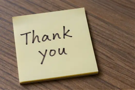 Close-up of 'Thank you' sticky note on wood cursive
