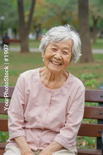 Elderly Asian Woman Smiling on Wooden Bench in Park
