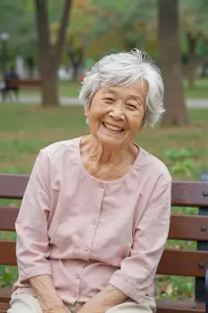 Elderly Asian Woman Smiling on Wooden Bench in Park