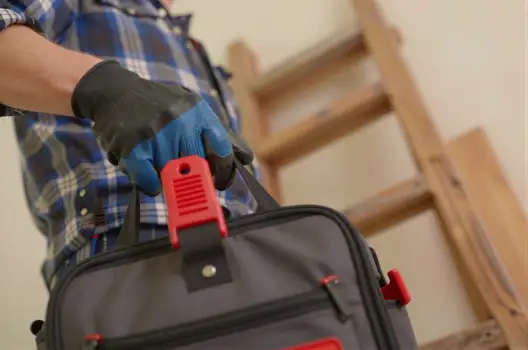 Hand Holding Tool Bag Against Wooden Ladder blue plaid shirt worker