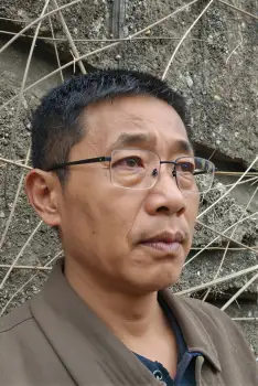 Middle-aged Asian man in brown jacket, serious expression