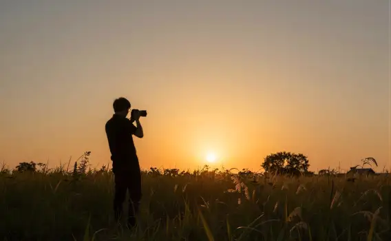Person Silhouette Taking Sunset Photo in Field