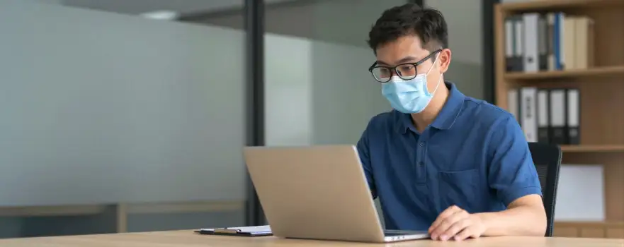 Young Man Working at Desk in Office laptop bookshelf