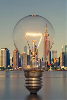 Light Bulb on Reflective Surface Against City Skyline at Sunset