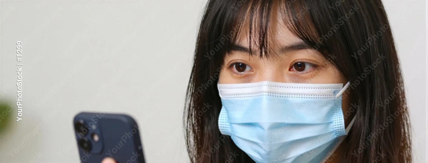 Young woman in blue surgical mask holding smartphone