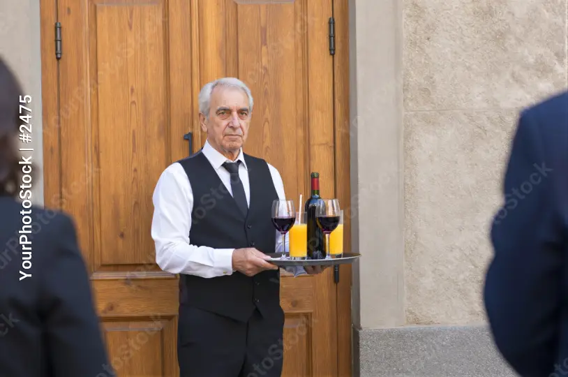 Elderly Man Holding Wine Glasses in Front of Wooden Door