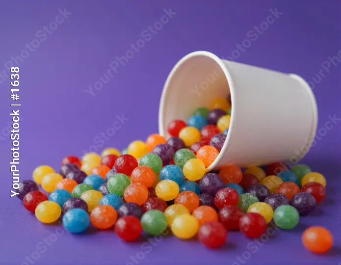 Colorful Jelly Beans Spilling from White Cup on Purple Surface