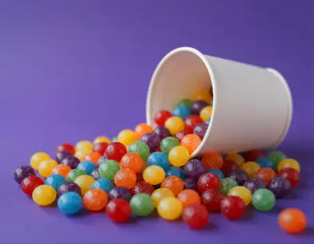 Colorful Jelly Beans Spilling from White Cup on Purple Surface
