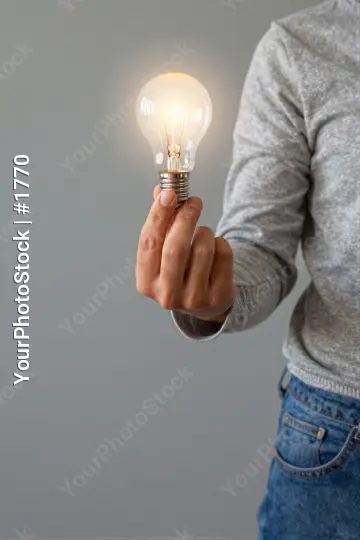 Hand Holding Light Bulb illuminated grey background