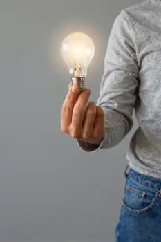 Hand Holding Light Bulb illuminated grey background
