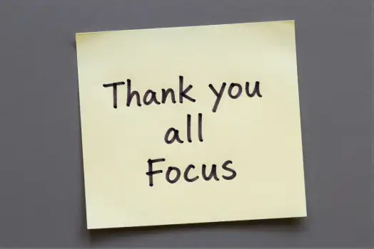 Yellow sticky note with 'Thank You All Focus' on gray surface