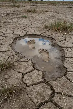 Circular puddle of water in cracked earth with footprints