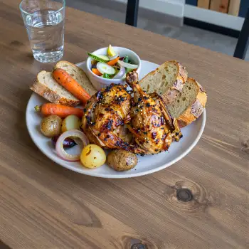 White round plate with roasted chicken and vegetables on wooden table