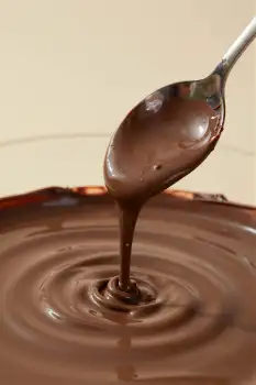Silver Spoon Pouring Melted Dark Chocolate into Bowl