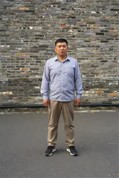Middle-aged man in front of brick wall looking serious asian