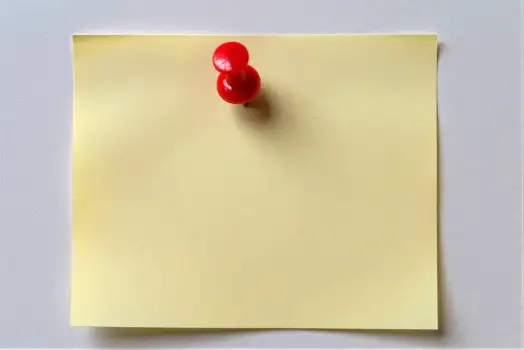 Yellow Sticky Note with Red Push Pins on White Wall