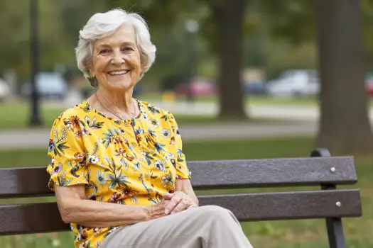 Elderly Woman Smiling on Wooden Bench in Park