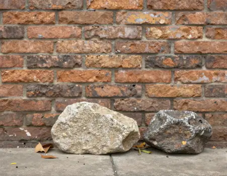 Two Large Rocks on Ground in Front of Weathered Brick Wall
