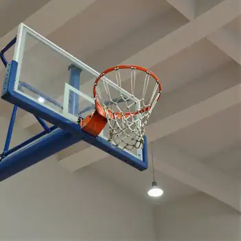 Dunking basketball hoop in gymnasium ceiling blue