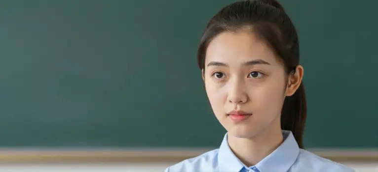 Serious Asian Woman Standing in Front of Green Chalkboard