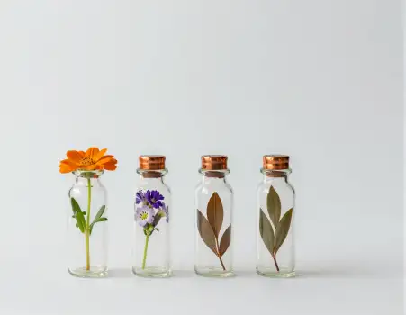 3 Small Glass Bottles with Copper Lids and Flowers on White Background