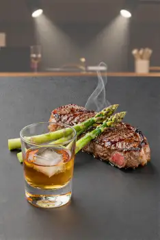Medium-Rare Steak with Asparagus and Whiskey on Black Countertop