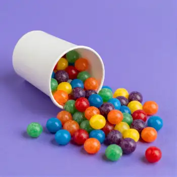 Colorful Candies Spilling Out of an Empty White Cup on Purple