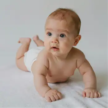 Baby lying on stomach on white blanket curious