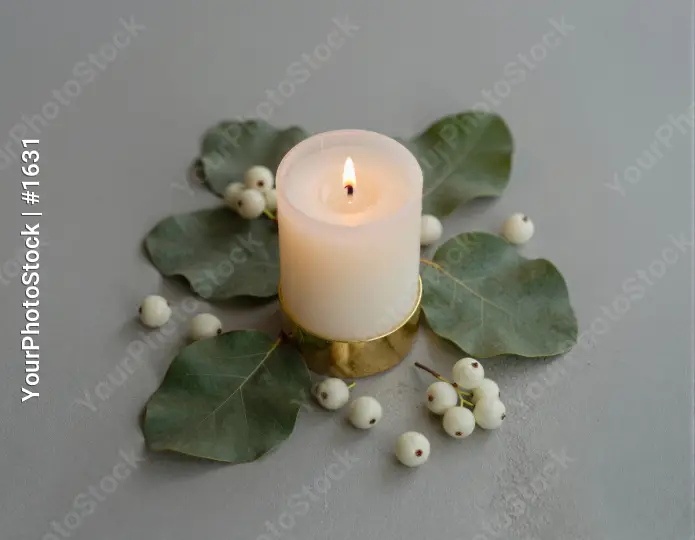 Lit White Candle on Gold Base with Green Leaves and Berries
