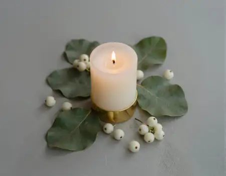 Lit White Candle on Gold Base with Green Leaves and Berries