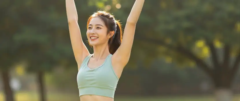 Happy young woman raising arms in park sunny day asian fitness