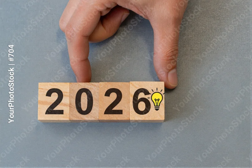 Hand Placing Wooden Block with Numbers 2026 on Blue Background