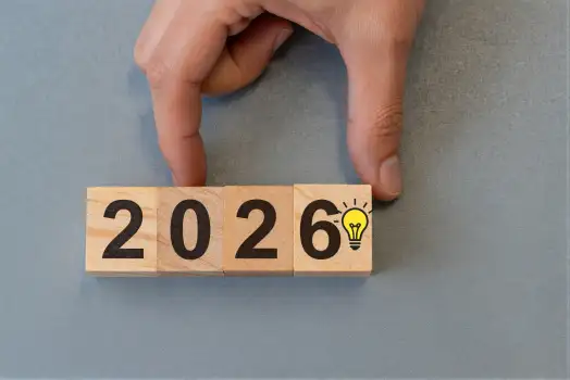 Hand Placing Wooden Block with Numbers 2026 on Blue Background
