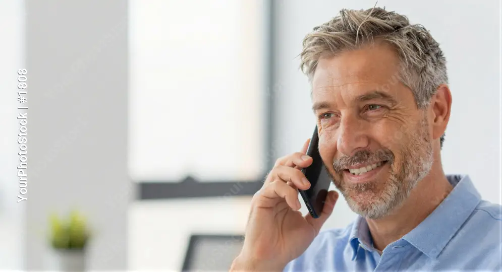 Middle-aged man smiling while talking on mobile phone in office