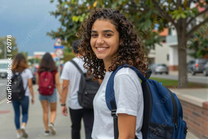 Happy young woman with curly hair walking on a sidewalk student university