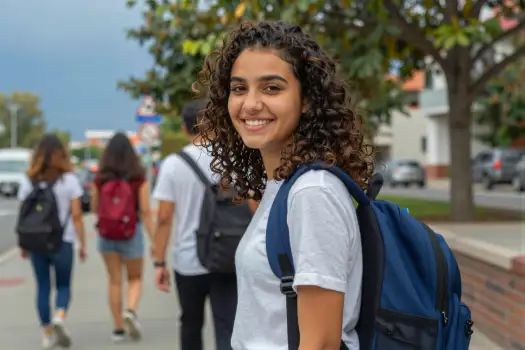 Happy young woman with curly hair walking on a sidewalk student university