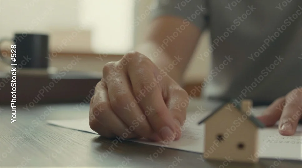 Hand Resting on Paper with Wooden House Model