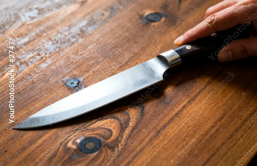 Close-up of a shiny knife blade on rustic wooden surface