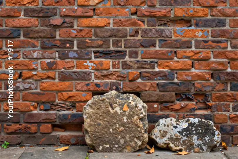 Weathered Brick Wall with Large Rocks and Fallen Leaves