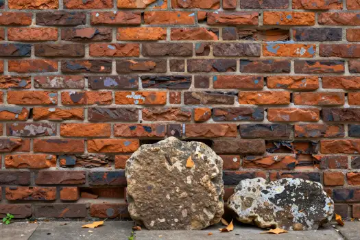 Weathered Brick Wall with Large Rocks and Fallen Leaves