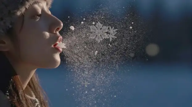 Young woman blowing snowflakes, winter scene hat