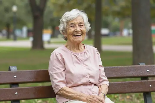 Elderly Woman Smiling on Wooden Bench in Park