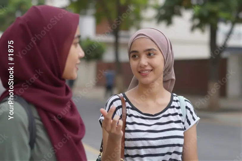 Two young women wearing headscarves conversing on the street