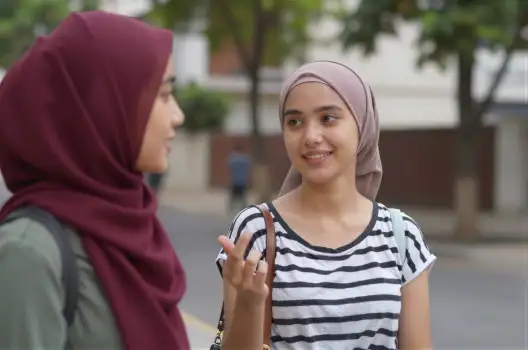 Two young women wearing headscarves conversing on the street
