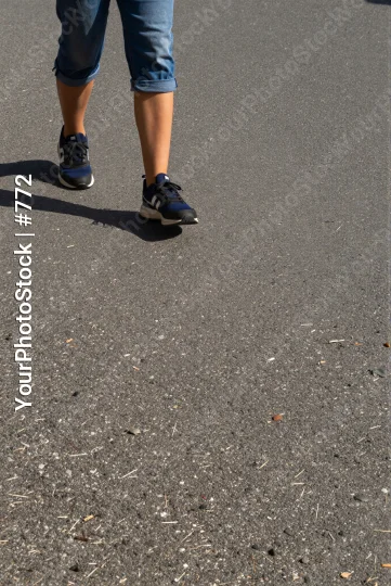 Person walking on road wearing blue jeans and black sneakers