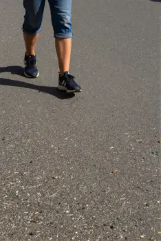 Person walking on road wearing blue jeans and black sneakers